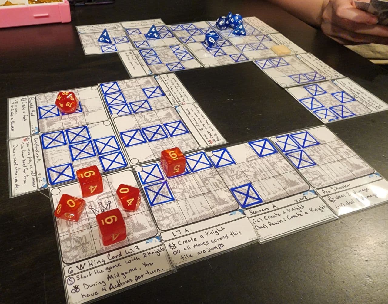 Prototype tiles laid out as a board mid-game, with hand-drawn patterns and red and blue dice as pieces